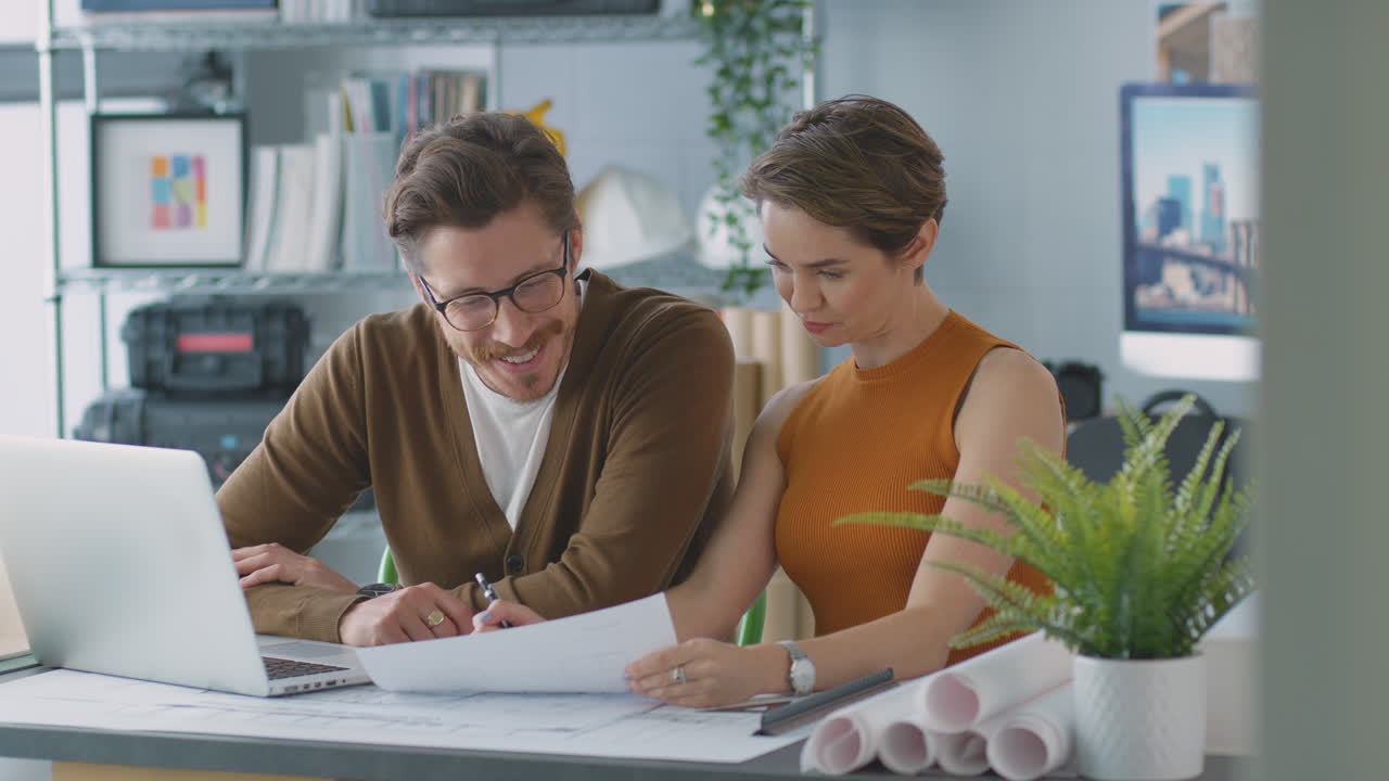 arquitectos masculinos y femeninos en la oficina trabajando en el escritorio en la computadora portátil y mirando los planes