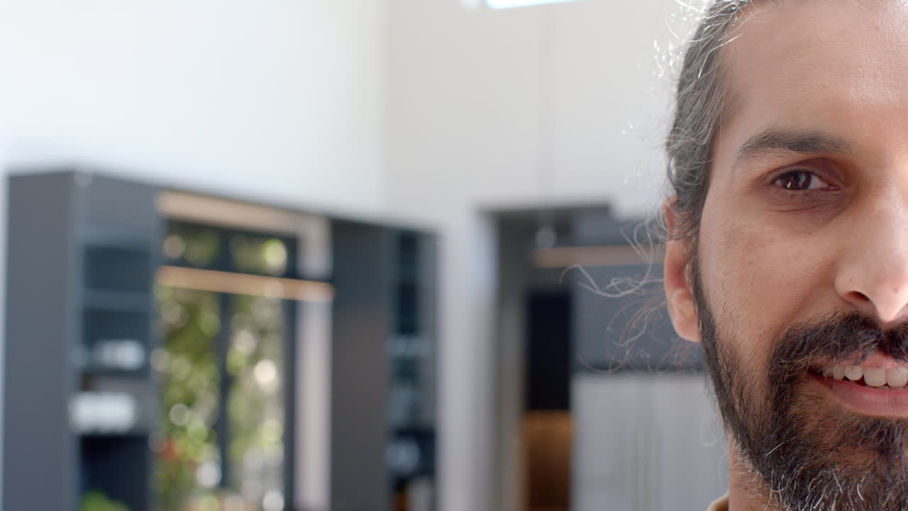 Smiling man with long hair standing in modern kitchen at home, copy space