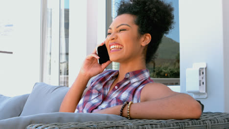 Side-view-of-young-mixed-race-woman-talking-on-mobile-while-sitting-in-balcony-at-home-4k