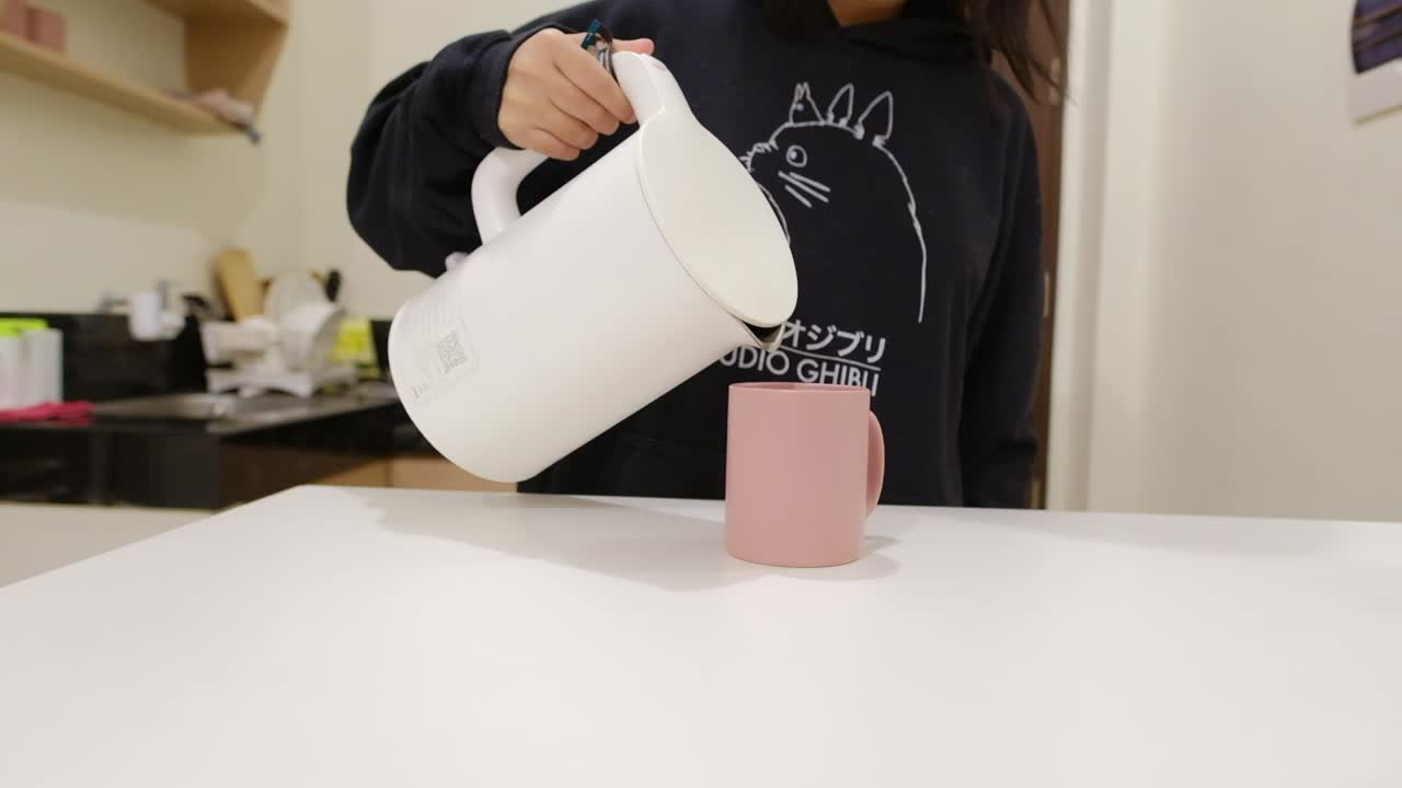 молодая девушка на кухне наливает воду в кружку.