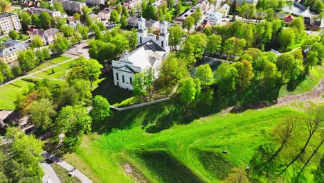 a white hilltop church stands prominently above lush spring trees and manicured green slopes, offering a tranquil view over a european town.