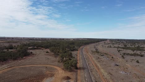 Drone-flying-over-unsealed-roads-and-a-railway-line-in-a-desert-style-landscape