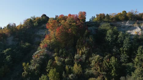 Drone-passing-through-a-hill-filled-with-trees-with-fall-colours-revealing-a-suburban-neighbourhood-down-the-horizon