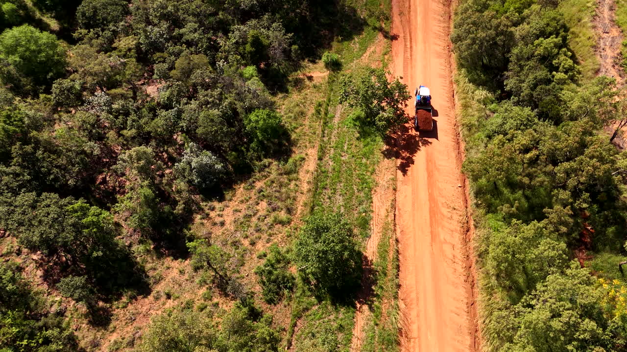 Veduta aerea dall'alto di un trattore che trasporta terra su una strada sterrata africana tra gli alberi