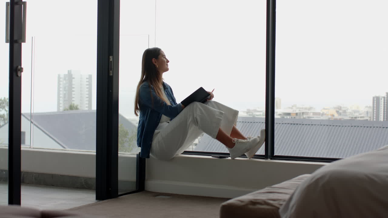 Relaxing at home, woman sitting by window reading book and enjoying view
