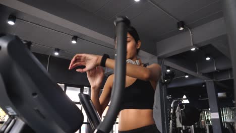 Young Asian woman running on a treadmill and looking at  clock in the health club