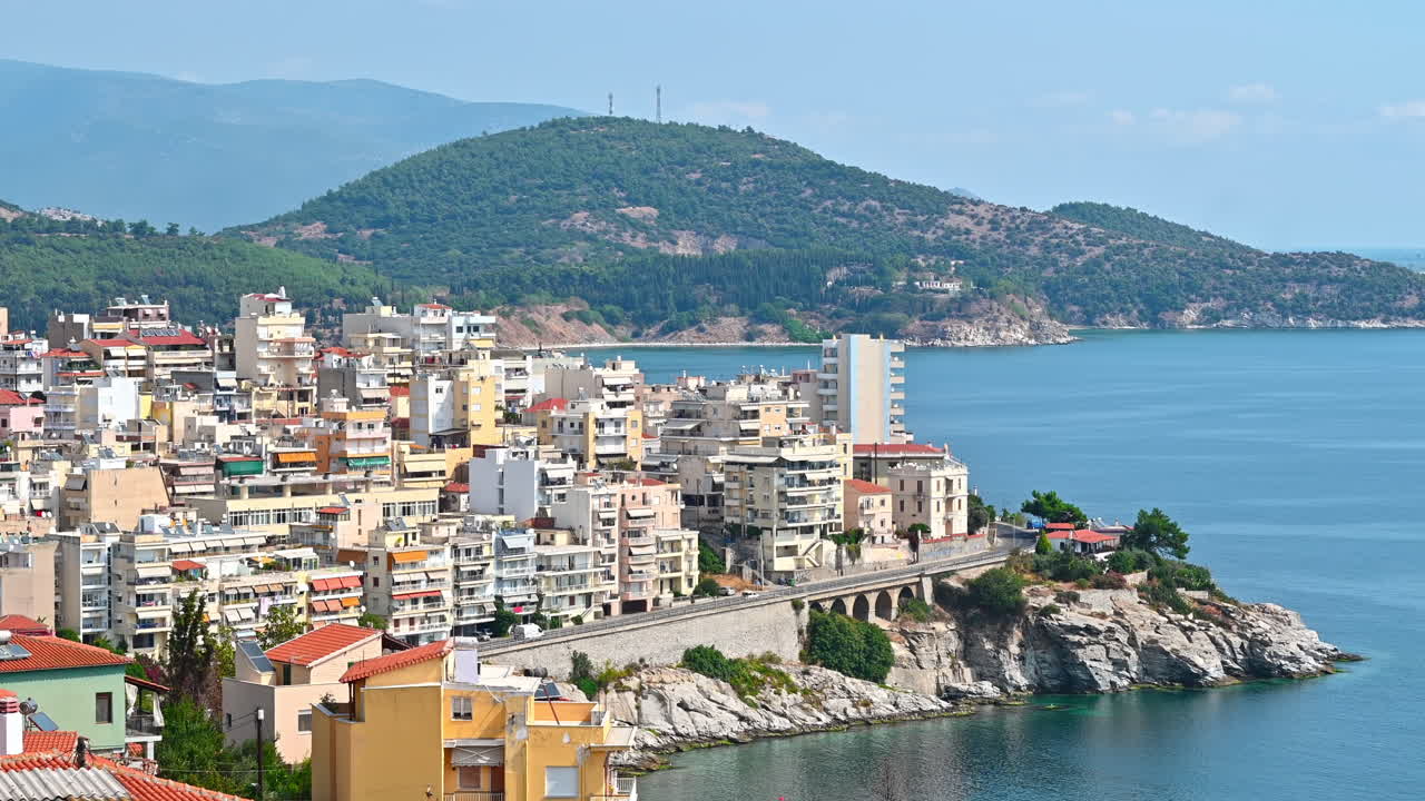Aerial view of Kavala. Rows of residential buildings, Aegean sea rocky coast, road with cars, hills on the background. Greece