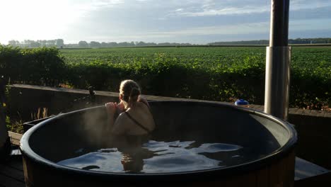 Woman-Admiring-Green-Field-Scenery-While-Bathing-In-A-Hot-Tub-Outdoor