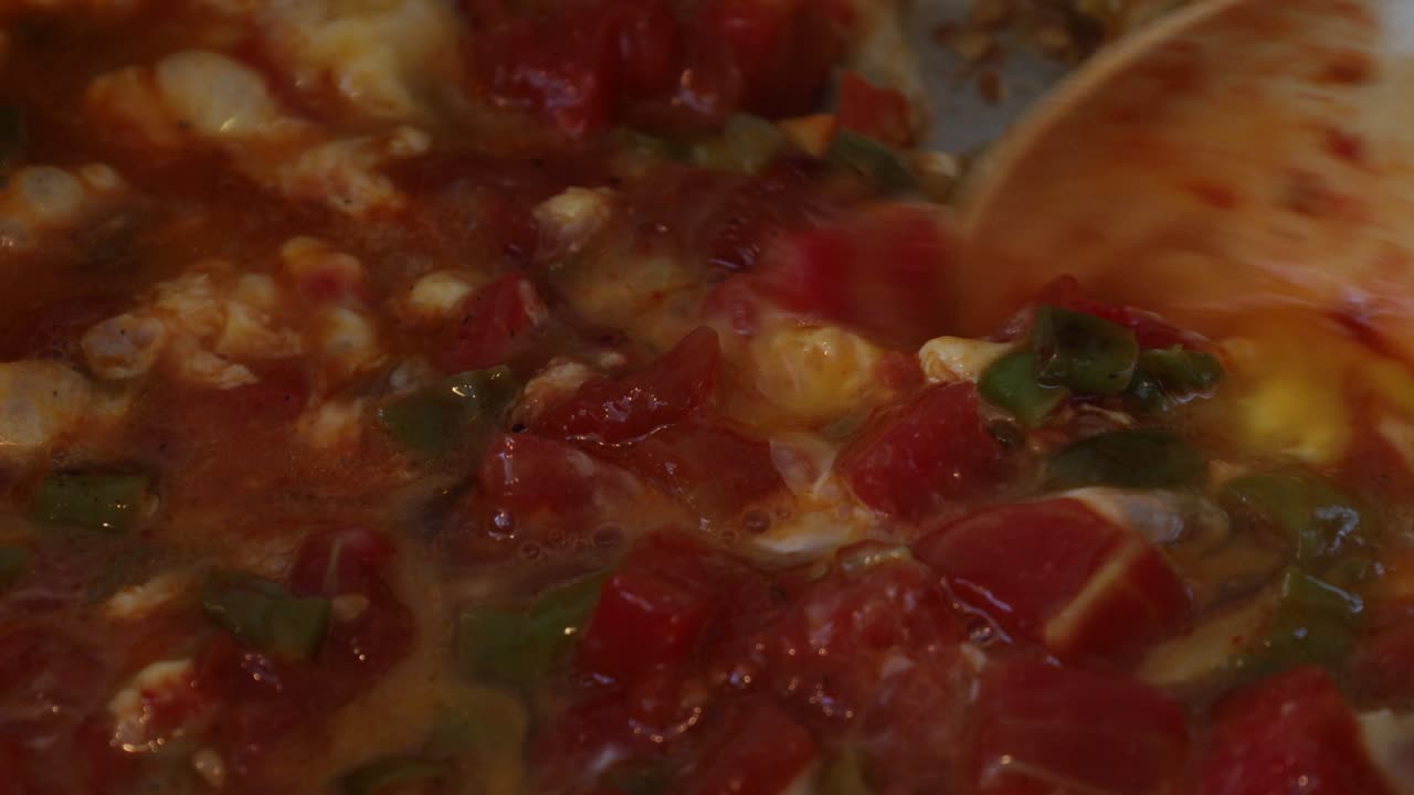 Ladle lifting hot stew showing ingredients like tomato, pepper and onion with cheese dripping