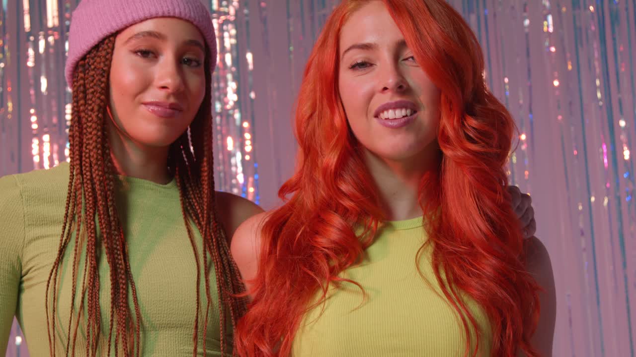 분홍색 배경에 틴셀 커튼 앞에 서 있는 두 명의 젊은 gen z 여성의 스튜디오 초상화