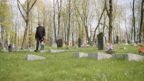 hombre triste con traje negro sosteniendo rosas rojas y caminando en un cementerio