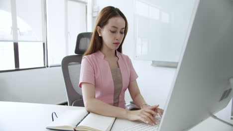 a young woman diligently types at her computer in a sleek modern office space.