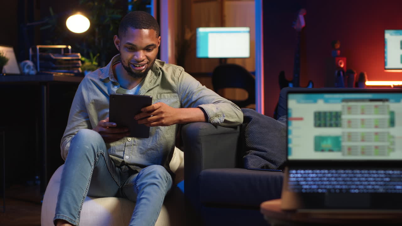 Video verticale: Lavoratore remoto nero che naviga sul tablet accanto a uno schermo che mostra analisi.