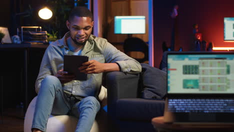 vertical video black remote worker navigating on tablet next to screen running analytics