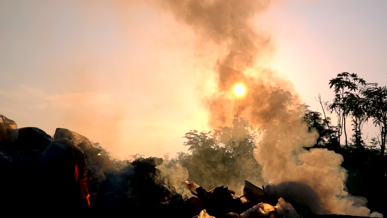 서서히 움직이는 불은 해가 뜨는 어두운 배경에서 쓰레기 봉투를 태우고 있습니다.
