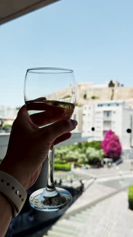 glass of white wine held up against an athens view