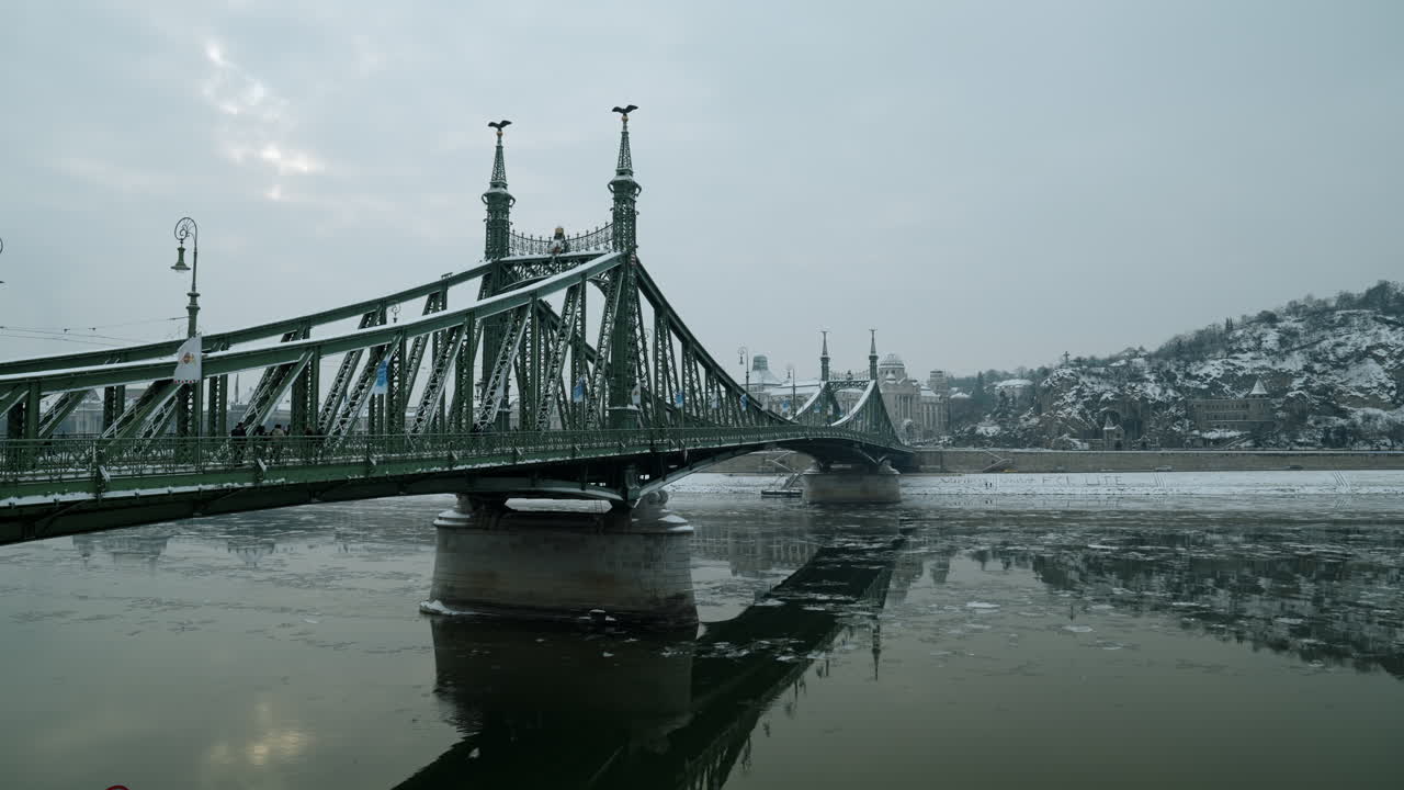 Vista invernale del Ponte della Libertà sul fiume Danubio a Budapest, con acqua ghiacciata, luce soffusa e architettura storica che creano una tranquilla atmosfera urbana europea durante la stagione fredda.