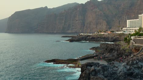 evening sun casts light on los gigantes as tourists watch crashing waves