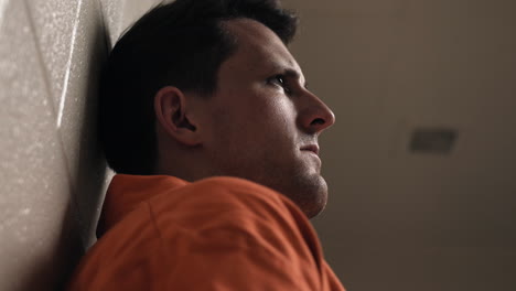 a sad, depressed attractive, handsome man, criminal prisoner, inmate in orange jumpsuit sitting in prison cell thinking, pondering, about to cry