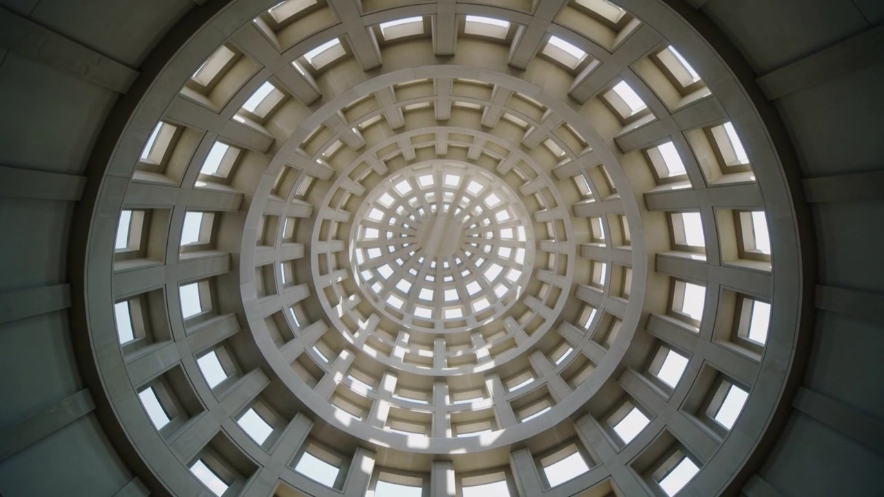 Telecamera che ruota e zooma, puntata verso l'alto su una cupola a cassettoni in una sala, mostrando lucernari quadrati e un oculo.