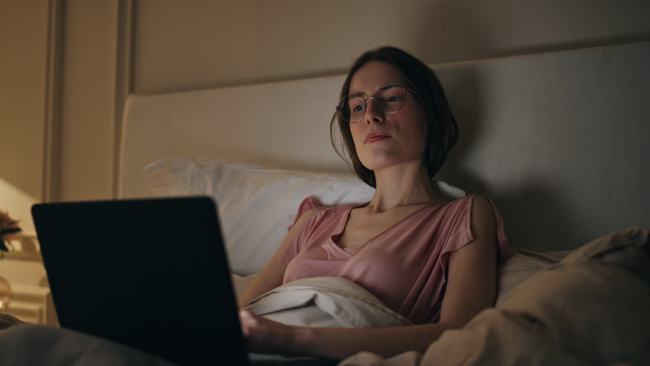 Primo piano di freelancer concentrato che lavora a letto cercando idee. Ragazza che digita al laptop a tarda ora.
