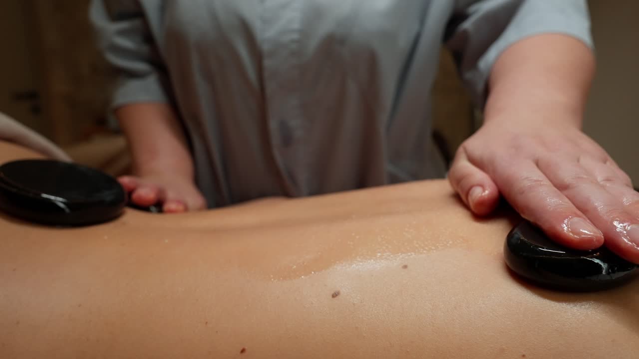 Massør udfører hot stone massage på kvindes ryg