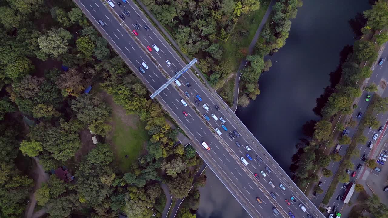busy highway traffic crossing a bridge over a river surrounded by trees. Unique aerial view flight vertical bird's eye view drone