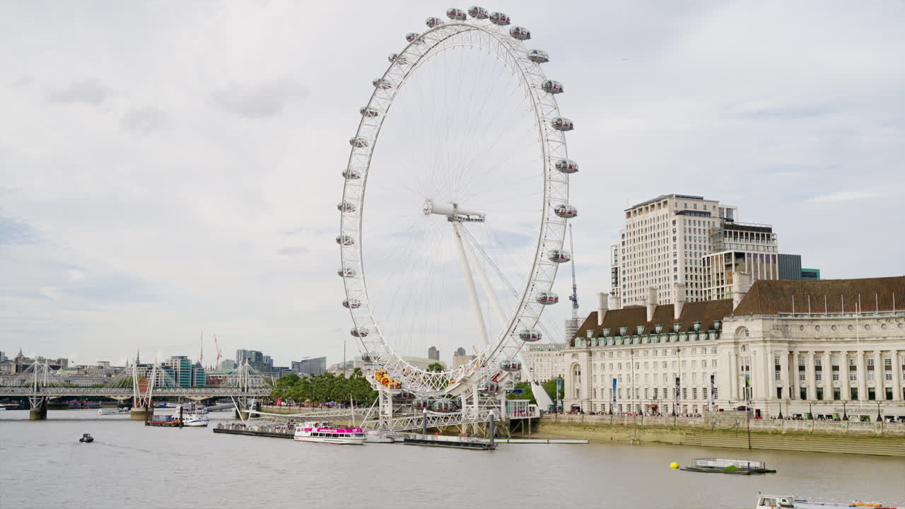 View of the London Eye ferris wheel in London downtown, United Kingdom. Queen's walk and Thames river with floating boat, cityscape on the background
