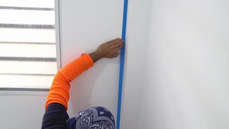 a man is placing blue masking tape on the wall to ensure that the painting lines are clean and precise - close up