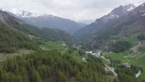 Scenic-Italian-Alpine-valley-green-meadows-forests-snowy-mountains-AERIAL