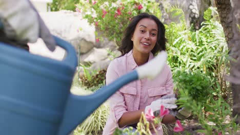 Feliz-Mujer-Birracial-Haciendo-Jardinería,-Plantando-Flores-Mientras-Su-Pareja-Regaba-Plantas