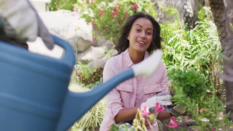feliz mujer biracial jardinería, plantar flores mientras su pareja regar las plantas