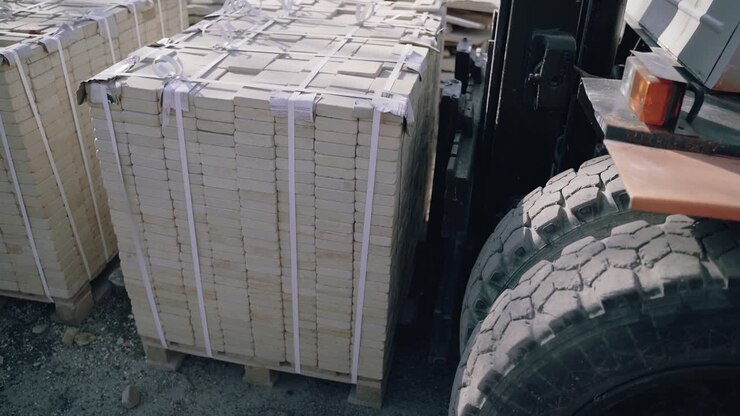 Un carrello elevatore sta sollevando un pallet di mattoni e lo porta via nel cortile della fabbrica.