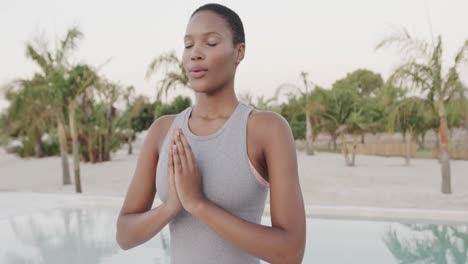 Relaxed-biracial-woman-practicing-yoga,-meditating-on-beach,-slow-motion