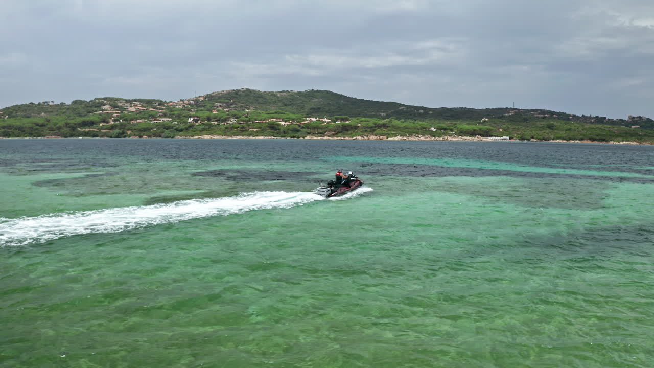 Jet skier glides over clear turquoise waters with lush green hills in the background