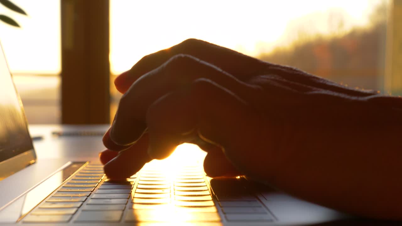 SLOW MOTION, CLOSE UP: Hands typing on laptop keyboard in early morning sunlight