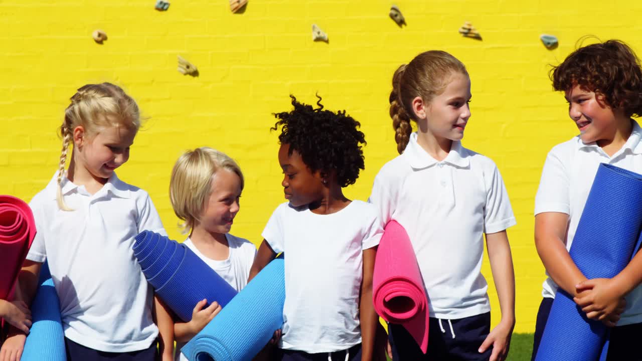 School kids holding yoga mat and interacting with each other