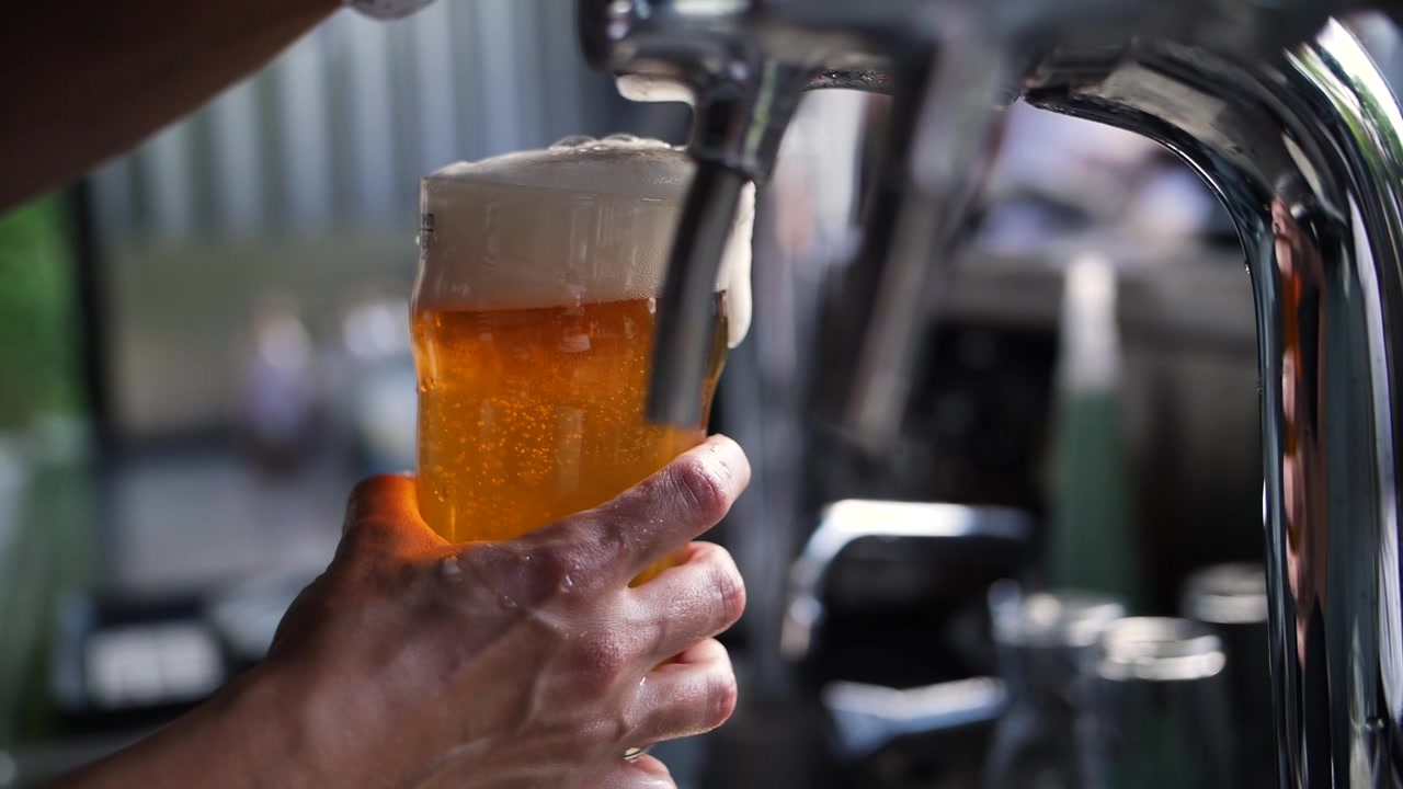 Barista che versa una pinta di birra dorata a una festa in giardino, in super slow motion.