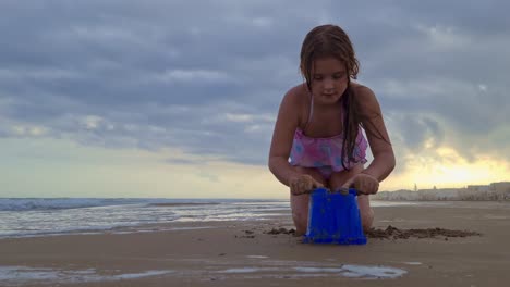 Niedriger-Winkel-Des-Schönen-Kaukasischen-Kleinen-Mädchens,-Das-Mit-Eimer-Und-Sand-Am-Strand-Spielt