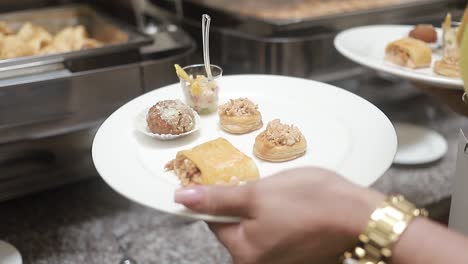 young girl holds a plate of buffet food with various sweet appetizers, camera closed