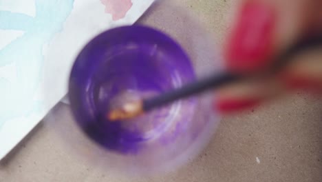 pincel disolviendo el color púrpura en un vaso de agua