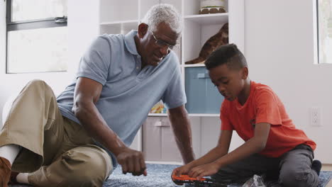 grandfather with grandson sitting on rug at home building model helicopter together
