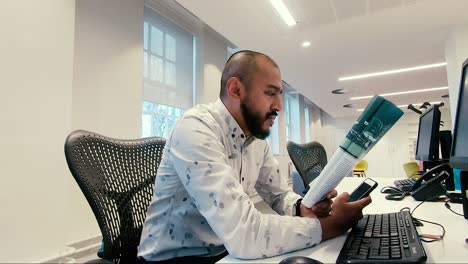 Asian-Indian-male-reading-magazine-at-office-desk