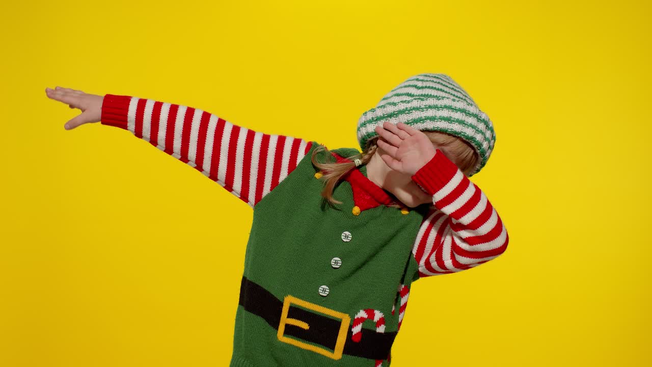 Bambina in costume da elfo aiutante di Babbo Natale che balla, esegue la dab dance, un gesto meme di internet.
