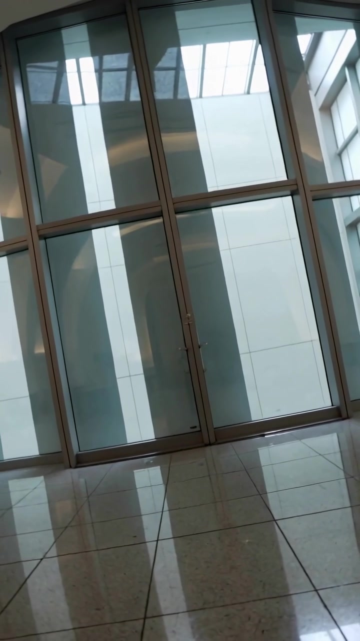 Video vertical: Cámara inclinándose y moviéndose hacia las puertas de cristal del vestíbulo, centrando los reflejos del suelo.