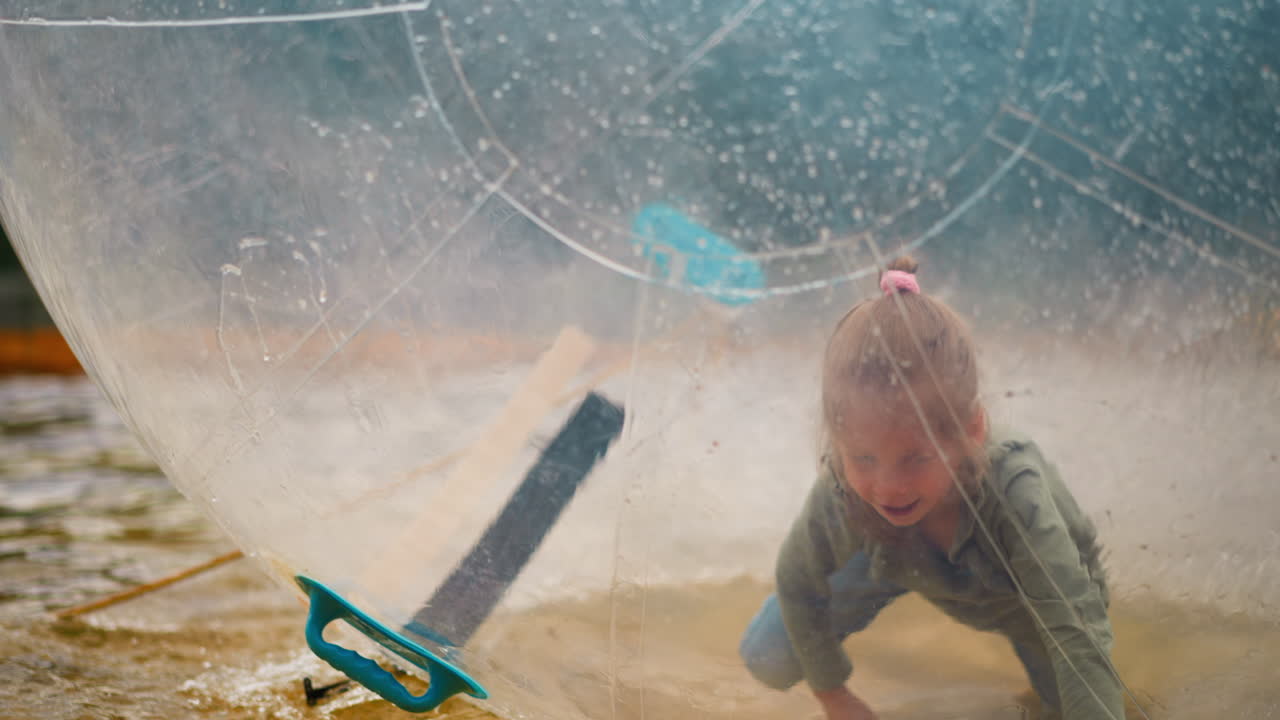 작은 수영장에서 떠다니는 물 공 안에 작은 소녀가 기어 들어갑니다.