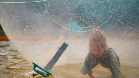 little girl crawls inside water ball floating in small pool