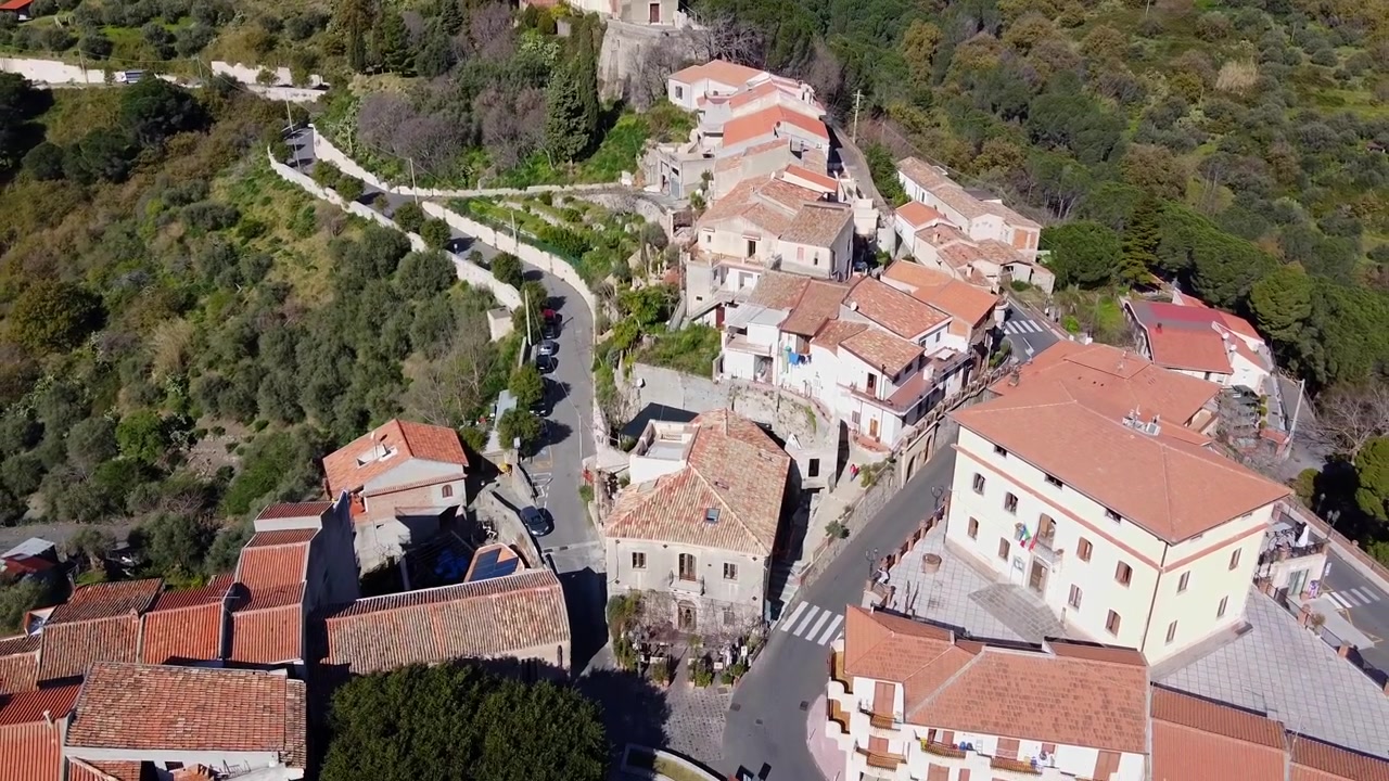 Borgo medievale collinare di Savoca in Sicilia, il famoso Bar Vitelli in Piazza Fossia come location delle riprese de Il Padrino, edifici rustici a picco sulla scogliera circondati da una lussureggiante valle verde, Sicilia, ripresa con drone.