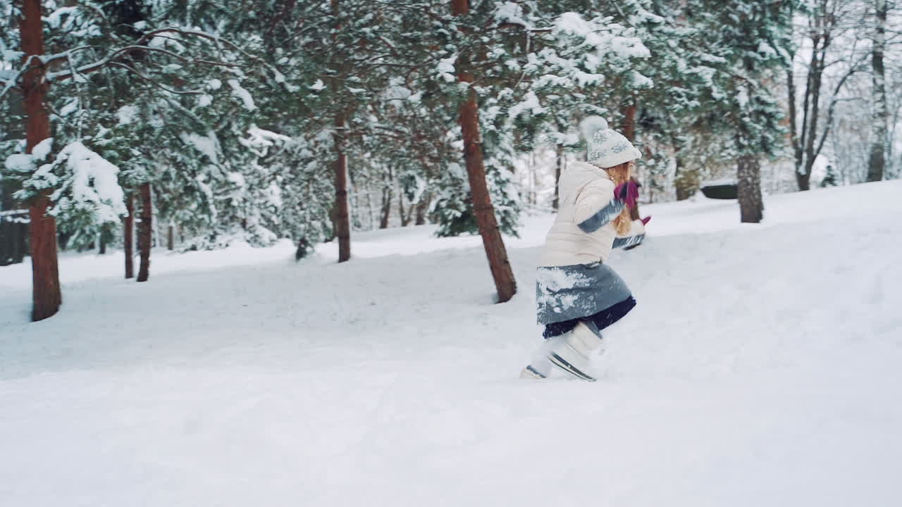 Little girl is running in the snow and falling into it in winter. Side view of a child who is having fun in cold season outdoors. Slow motion.