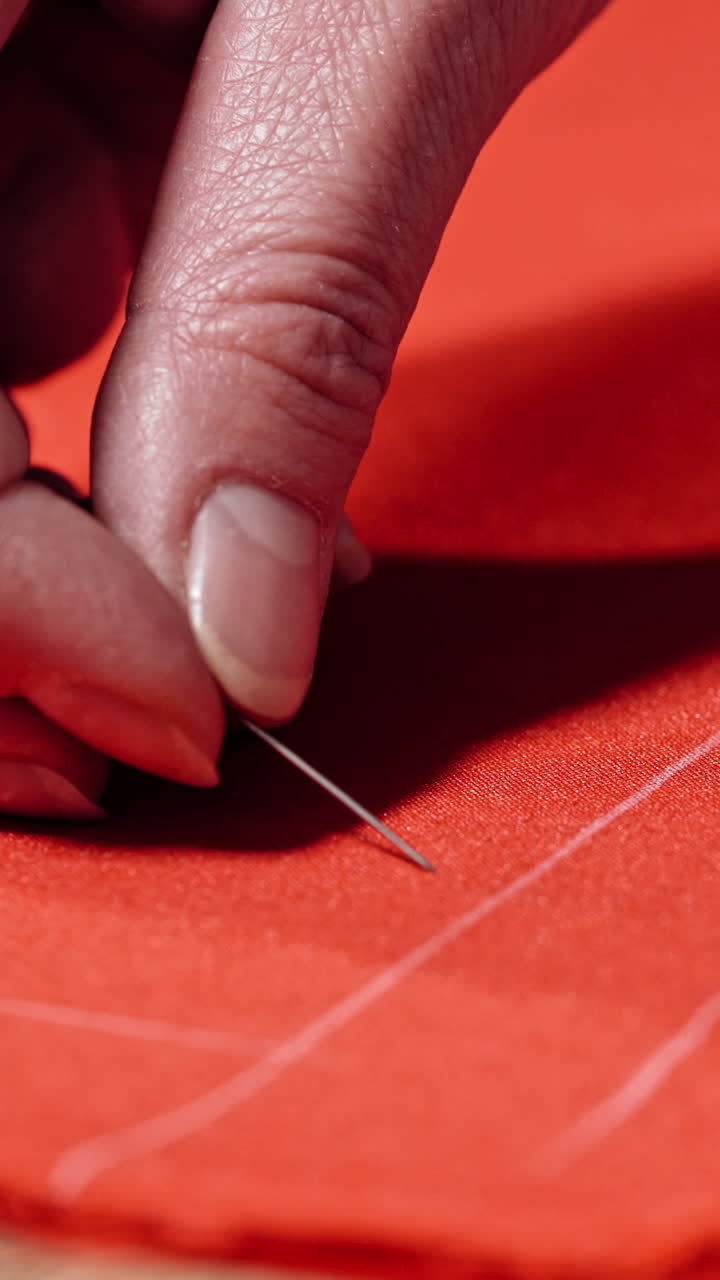 Female hands of the skilled worker putting the pin to the fabric. Red cloth with white lines and a tailor pinning the material on the table. Concept sewing and handicraft. Vertical video